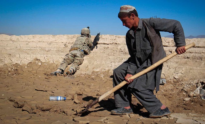 An Afghan boy works at a construction site behind a US Army soldier in Logar province, Afghanistan.