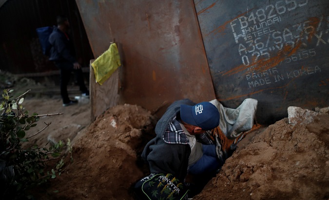 A migrant from Honduras, part of a caravan of thousands from Central America trying to reach the United States, crawls through a hole under a border wall to cross illegally from Mexico to the U.S in Tijuana.