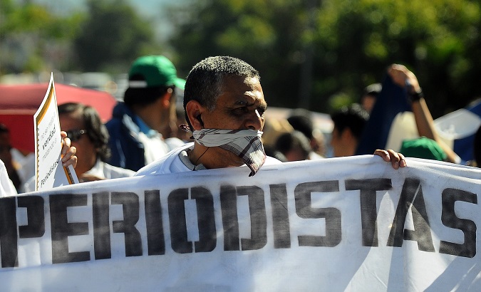 A protester wears a scarf over his mouth, symbolizing the state's censorship of the media, while holding a sign with the word 