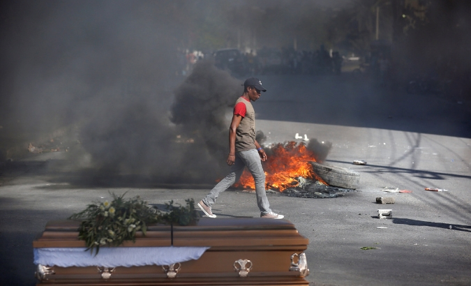 A man walks past burning tires and one of the caskets of victims of anti-government protests, placed in the street by relatives and fellow demonstrators, Haiti