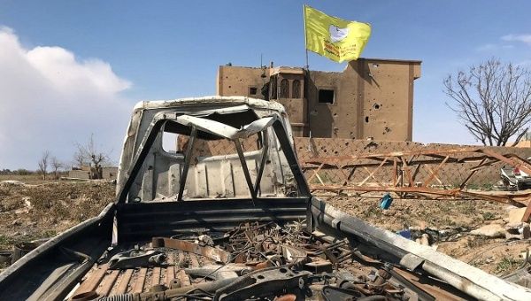 Syrian Democratic forces flag flutters on a damaged building in the village of Baghouz, Deir Al Zor province