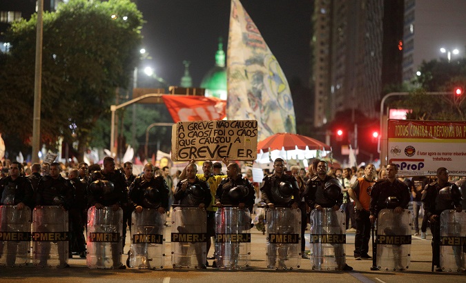 Riot police take up position in Rio de Janeiro, Brazil June 14, 2019. The sign reads: 'The strike did not cause chaos. It was the chaos that caused the strike.'