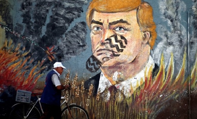 A Palestinian man walks with his bicycle past a mural depicting U.S. President Donald Trump, in Gaza City, June 24, 2019.
