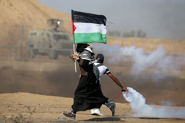 A woman holding a Palestinian flag runs as tear gas fired by Israeli forces during an-anti Israel protest, at the Israel-Gaza border fence in the southern Gaza Strip August 23, 2019.