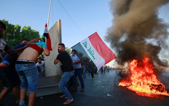 Demonstrators hold the Iraqi flag near burning objects at a protest during a curfew, three days after the nationwide anti-government protests turned violent, in Baghdad, Iraq October 4, 2019.