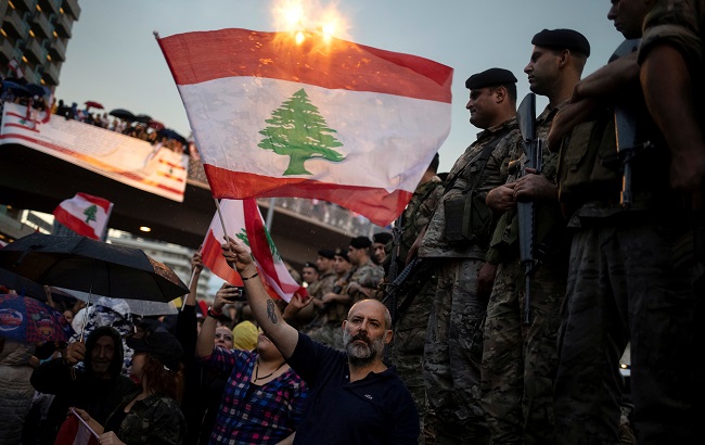 A demonstrator waves a Lebanese national flag next to Lebanese army soldiers during ongoing anti-government protests at a highway in Jal el-Dib, Lebanon, October 23, 2019.