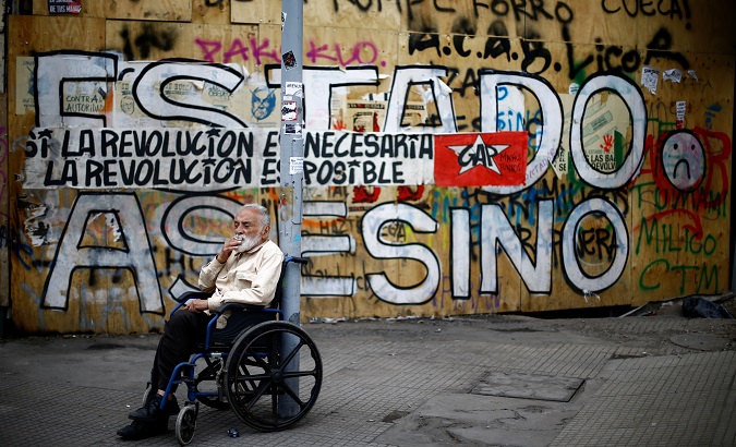 Retired journalist Jorge Vera protests in front of a wall reading 'Murderer state' and 'The revolution is necessary, the revolution is possible' in Santiago, Chile Nov. 1, 2019.