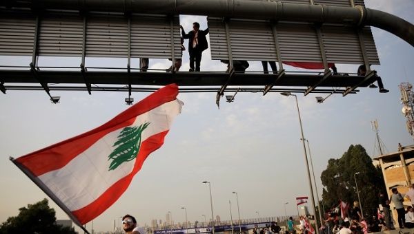 A protester waves a Lebanese flag as another one stands on a road sign at a demonstration blocking the highway during ongoing anti-government protests in Hazmiyeh, Lebanon November 13, 2019.