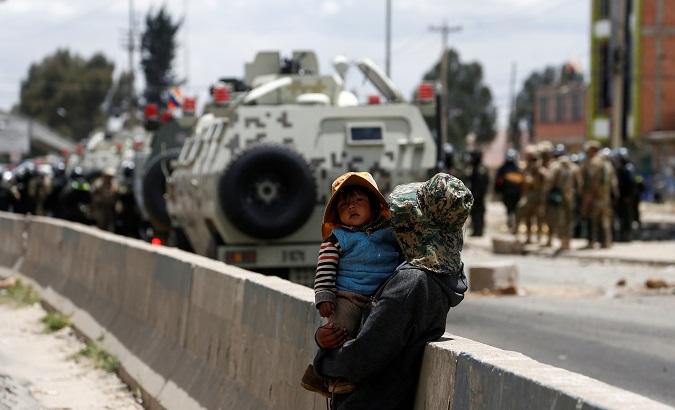 Woman carrying a child watches armed vehicles during a protest in Senkata, El Alto, Bolivia Nov. 19, 2019.