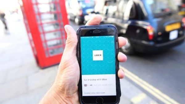 A photo illustration shows a London taxi passing as the Uber app logo is displayed on a mobile telephone, as it is held up for a posed photograph in central London September 22, 2017. 