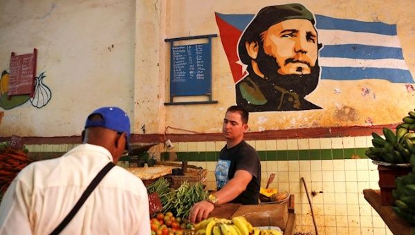 A man buys in an agromercado with the image of Fidel Castro painted on one of its walls