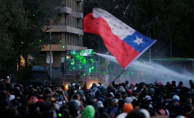 Demonstrators wave a Chile flag in front of a water cannon in Santiago, Chile, Jan. 10, 2020.