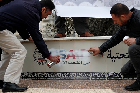 Palestinians spray paint to cover a logo of USAID in protest of Donald Trump's Middle East peace plan in Ramallah.