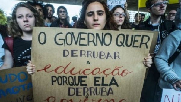 Woman holds a sign that reads ‘The government wants to overthrow education because education overthrows the government’.