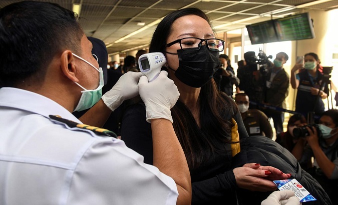 A health worker uses an infrared thermometer to check the temperature of a tourist