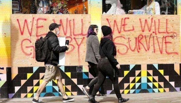 People walk by a boarded up window at a closed store with a message in the Haight-Ashbury district, 'We Will Get By, We Will Survive' in San Francisco, California, USA, 18 March 2020. 