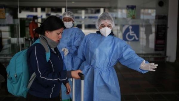 A staff member wearing a mask and protective suit guides a passenger at a coach terminal in Bogota, Colombia, March 24, 2020. 