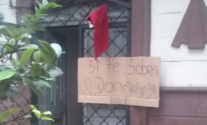 A red rag placed on a door. The sign reads, 'If you have something left over, donate it.' Colombia, April, 2020.