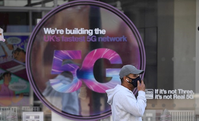 Person passes in front of a 5G tech advertisement, U.K., 2020.