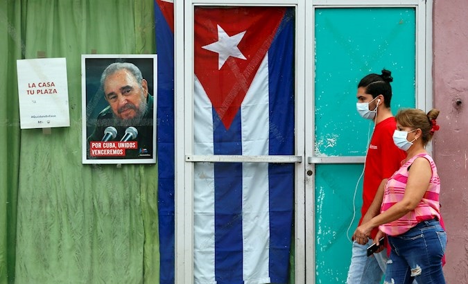 Two people walk in front of an image of Fidel Castro, Havana, Cuba, May 5, 2020.