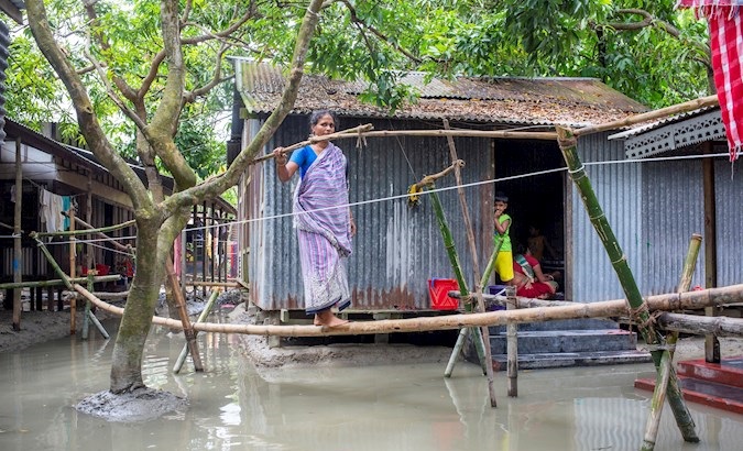 A woman crosses a makeshift bridge in a flood-affected area in Dohar, Dhaka, Bangladesh, August 6, 2020.