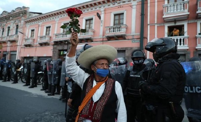 A protester holds a rose during a protest while police guard the march, Quito, Ecuador, Oct. 22, 2020.
