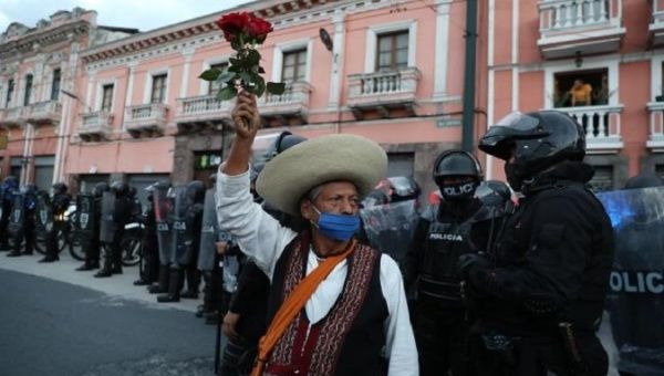 A protester holds a rose during a protest while police guard the march, Quito, Ecuador, Oct. 22, 2020.