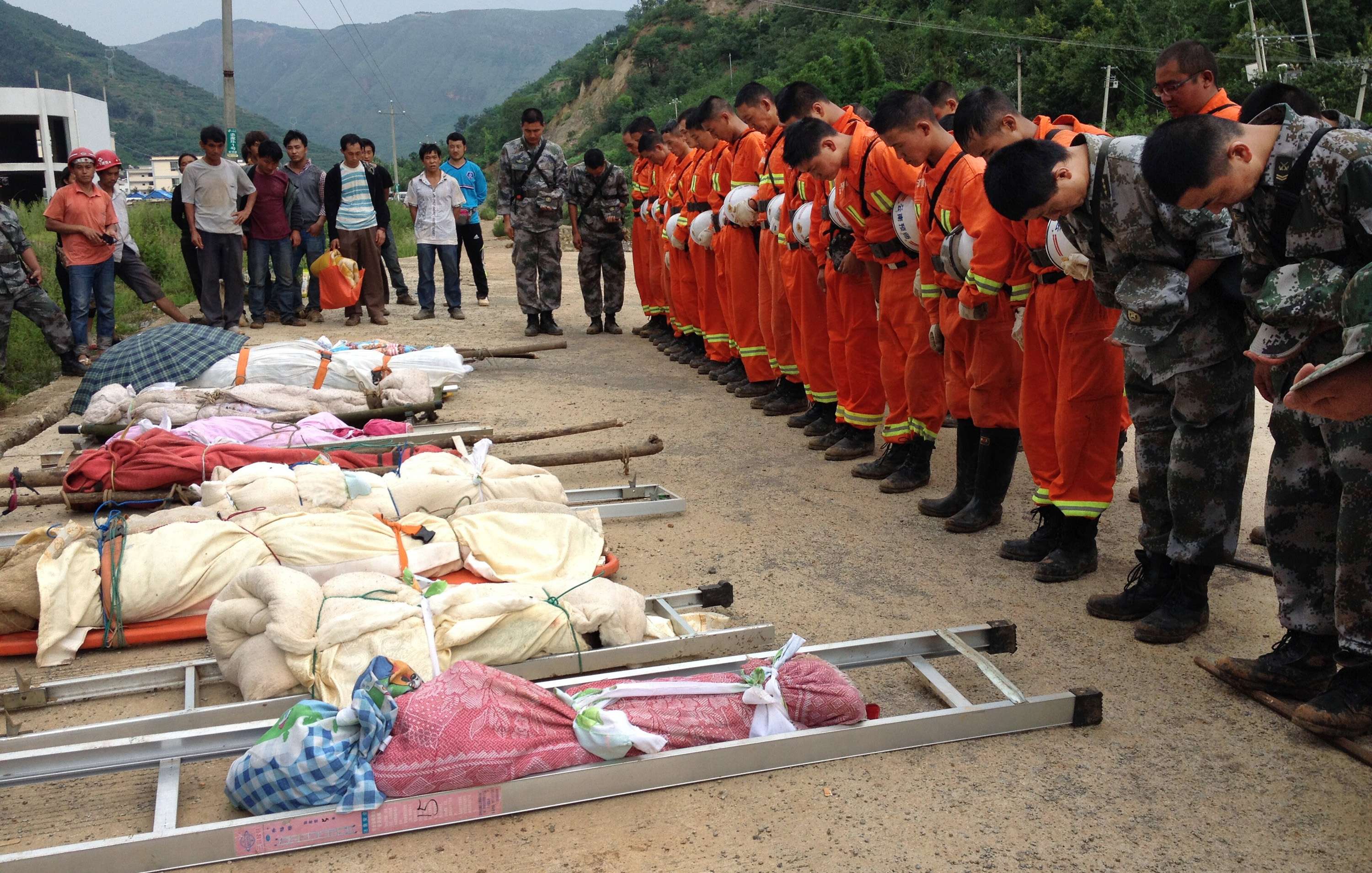 Rescuers (R) bow as they pay tribute to residents who were killed during the earthquake, Sunday (Photo: Reuters)