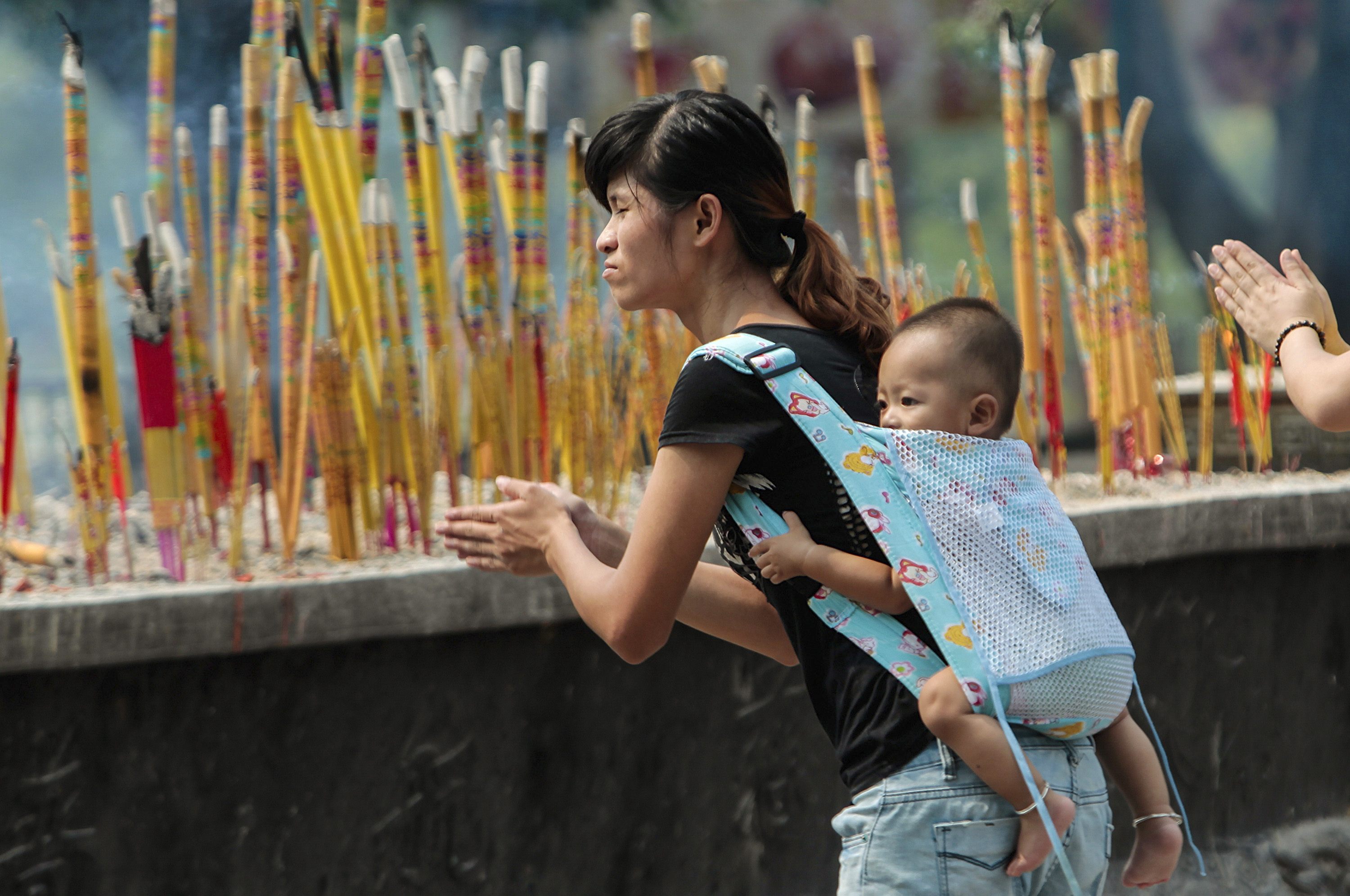 A woman carries her son on her back as she prays for those affected by Sunday's earthquake which hit Longtoushan town, at a temple in Guangzhou, Guangdong province, August 5, 2014. (Photo: Reuters)