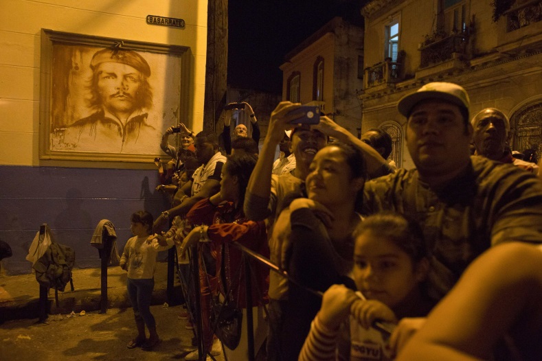 People watch a march in celebration of the 162nd birth anniversary of Cuba's independence hero Jose Marti beside an image of Cuban revolutionary hero Ernesto 'Che' Guevara on a wall in downtown Havana in Havana on January 27, 2015