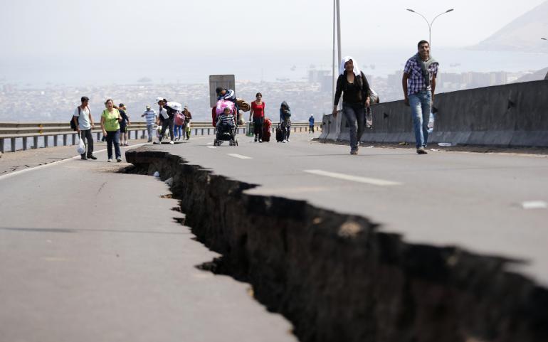 People walk next to a crack along a damaged road in the northern port of Iquique on April 3, 2014, after a powerful 8.2-magnitude earthquake struck off northern Chile.