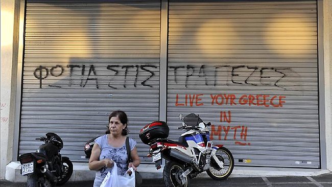 A woman stands by a bank in Athens, sprayed with slogans 