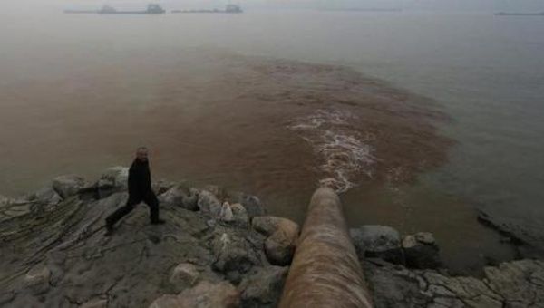 A man walks by a pipe discharging waste water into the Yangtze River from a paper mill in Anqing, Anhui province, Dec. 4, 2013.