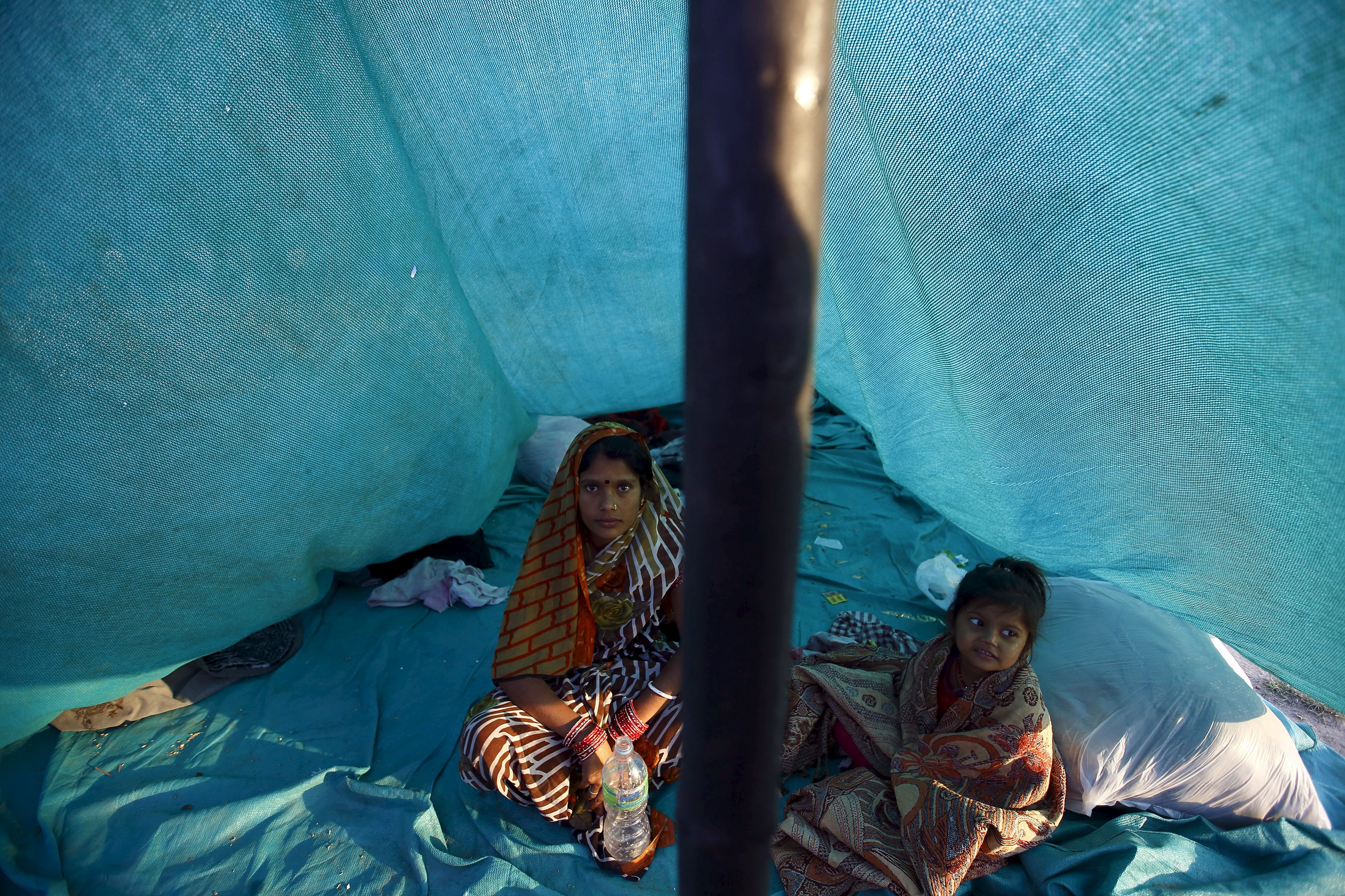 A mother and her child sit inside a makeshift shelter in an open ground to keep safe after the earthquake in Kathmandu, Nepal April 26, 2015.