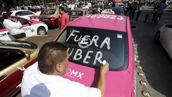 A Mexico City taxi driver writes the slogan “Uber Out” on his cab during mass protests against private car services May 25, 2015.