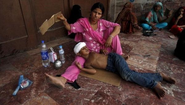 A woman uses a piece of cardboard to fan her son, while waiting for their turn for a medical checkup during intense hot weather in Karachi, Pakistan, June 23, 2015.