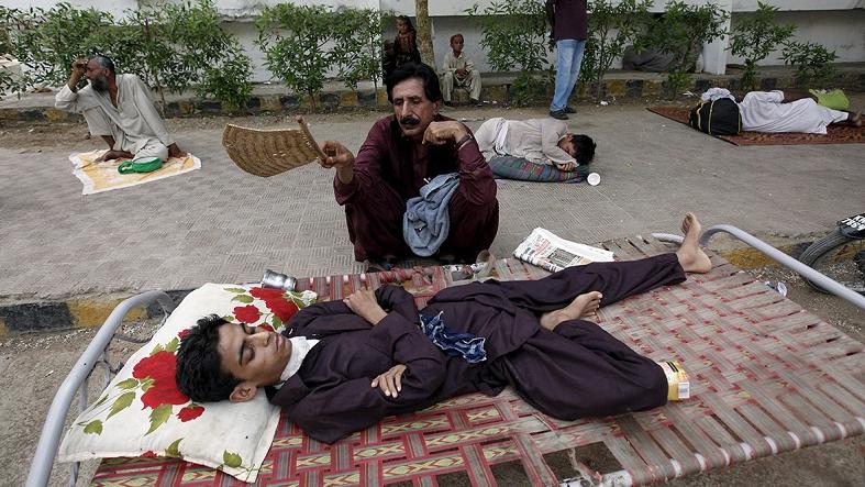 A man uses a handheld fan to cool down his son, while waiting outside Jinnah Postgraduate Medical Centre in Karachi.