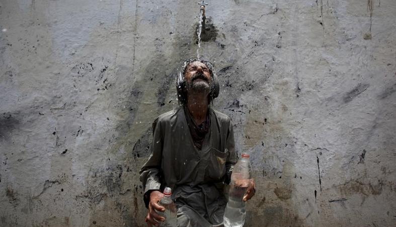 A man cools off from a public tap after filling bottles during intense hot weather in Karachi, Pakistan, June 23, 2015.