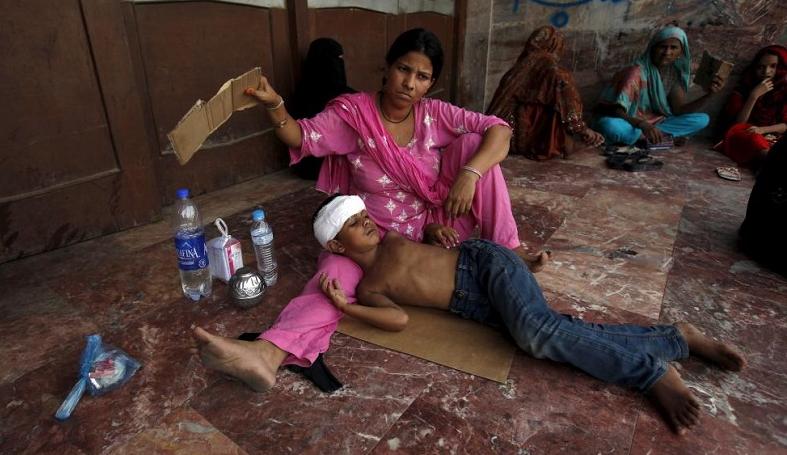 A woman uses a piece of cardboard to fan her son, while waiting to be seen Jinnah Postgraduate Medical Centre in Karachi.