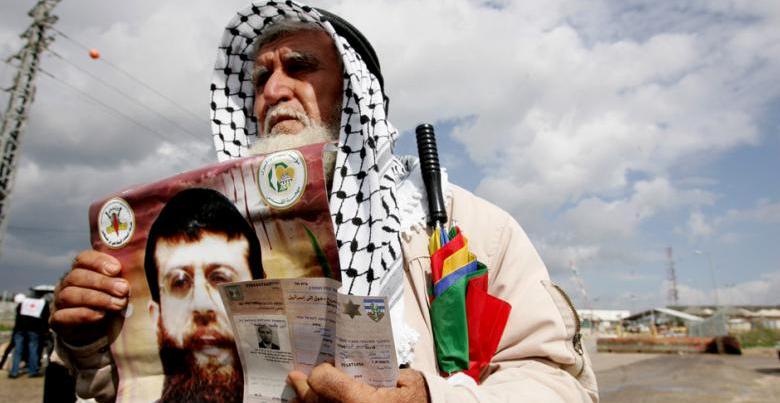 The father of former Palestinian prisoner Khader Adnan holds a poster of his son and an ID, 19 February 2012.