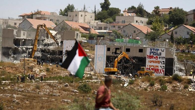 A Palestinian flag as Israeli heavy machinery demolish apartment blocs in the West Bank Jewish settlement of Beit El July 29, 2015.