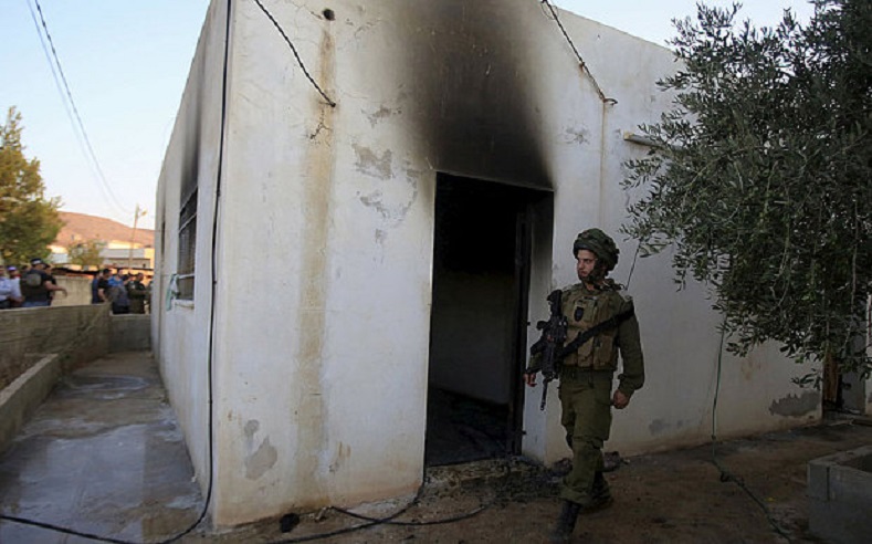 An Israeli soldier walks past a house that had been torched in a suspected attack by Jewish extremists, Nablus July 31, 2015.