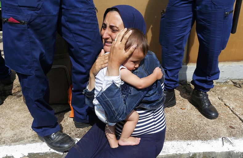 Hungarian policemen stand by a refugee holding a baby at the railway station in the town of Bicske, Hungary, September 3, 2015. A camp for refugees and asylum seekers is located in Bicske. 