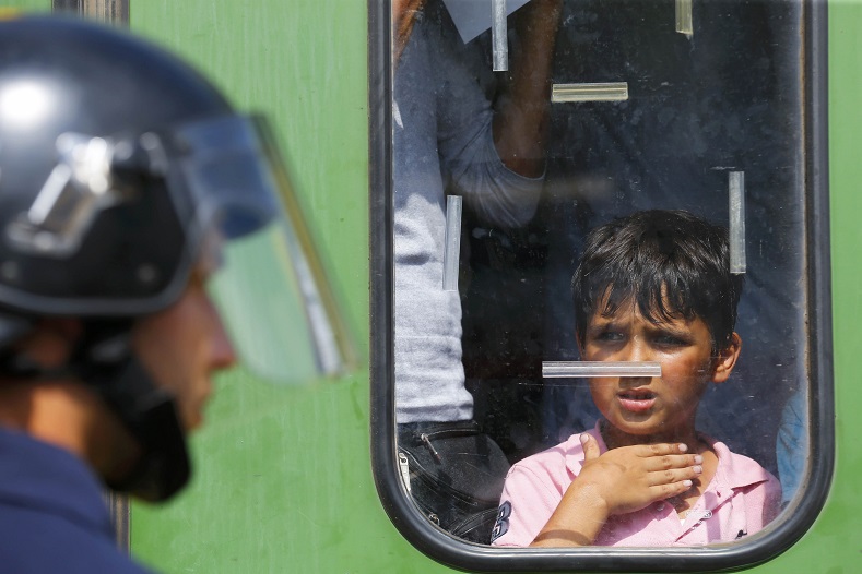A refugee boy looks at a Hungarian policeman at the railway station in the town of Bicske, Hungary, September 3, 2015. A camp for refugees and asylum seekers is located in Bicske. 