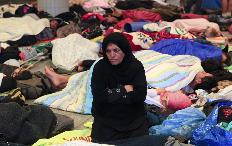 A woman sits among sleeping migrants near the Keleti railway station in Budapest, Hungary, September 3, 2015. Over 2,000 migrants, many of them refugees from conflicts in the Middle East and Africa, had been camped in front of the Keleti Railway Terminus, closed to them by authorities saying European Union rules bar travel by those without valid documents. 