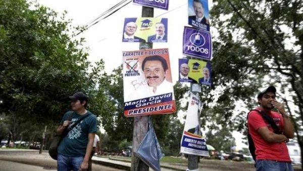 People stand near campaign signs at a bus stop before Sunday's presidential election in Guatemala City.