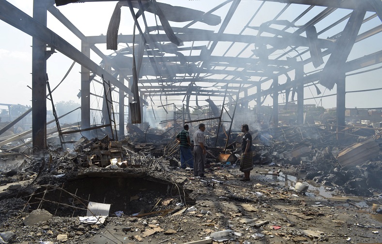 Men walk at the site of a Saudi-led air strike targeted at Public Electricity Corporation branch in Yemen's western city of Hodeidah October 11, 2015.