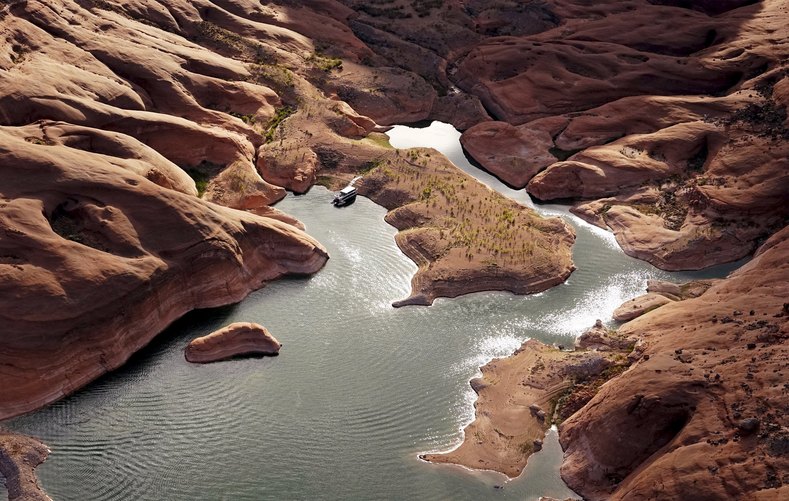 A houseboat camps on the shore in shallow water in a canyon at Lake Powell.