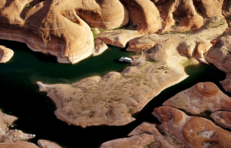 A houseboat camps on the shore in shallow water in a canyon at Lake Powell.