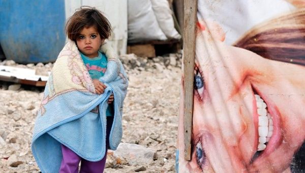 A young Syrian refugee covers herself with a blanket as she stands outside tents at a makeshift settlement in Bar Elias in the Bekaa valley